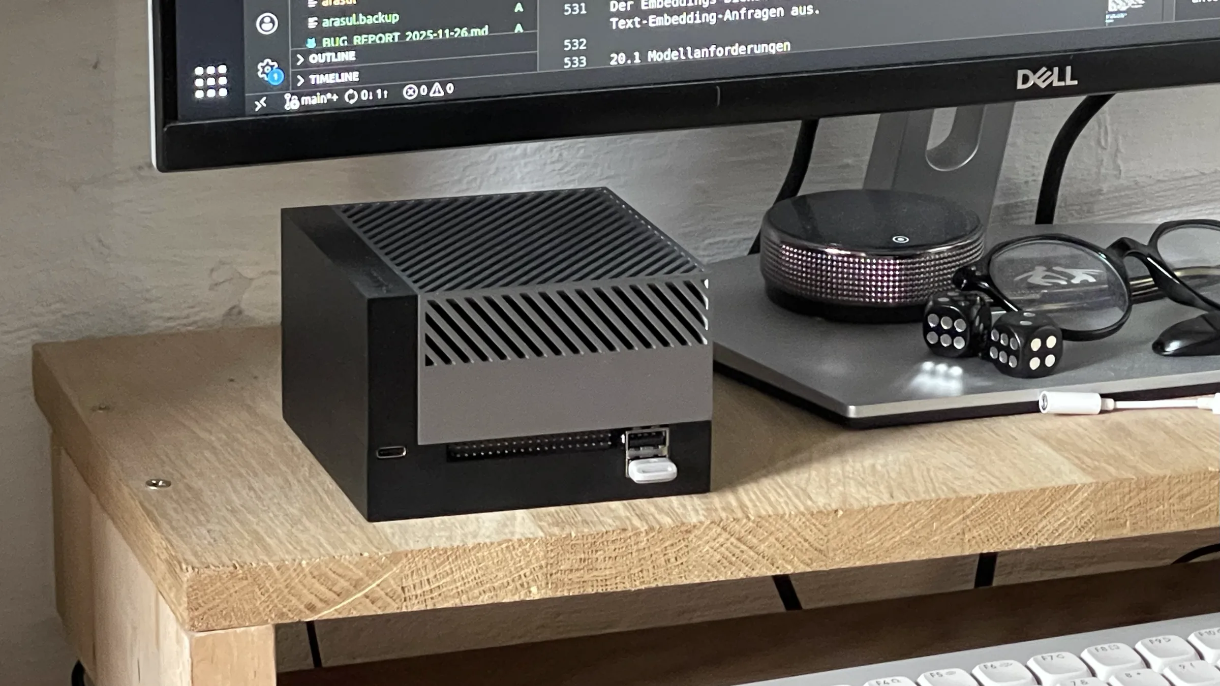 Compact AI machine running Ara OS on a desk, with a monitor showing an open editor behind it
